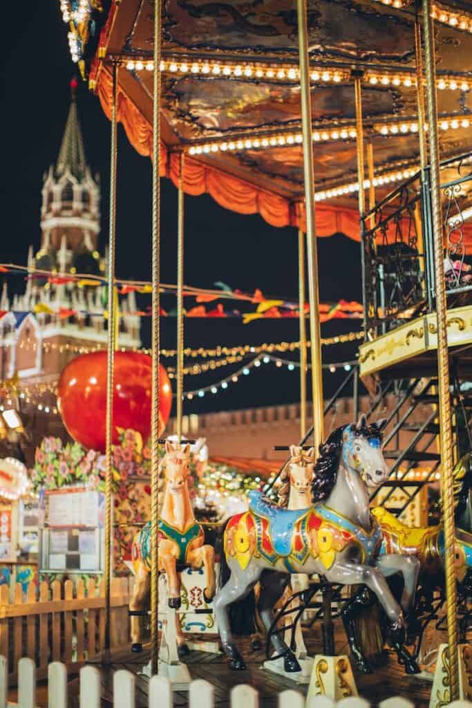 Festive merry go round with carnival horses on Red Square against blurred Kremlin during New Year holidays in evening