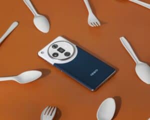 Oppo smartphone surrounded by white spoons and forks on a brown surface.
