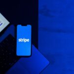 A smartphone displaying the Stripe app placed on a laptop keyboard with a blue monochromatic tone.